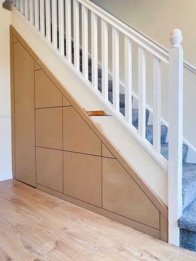 A wooden door built into the wall under a staircase with white railings.